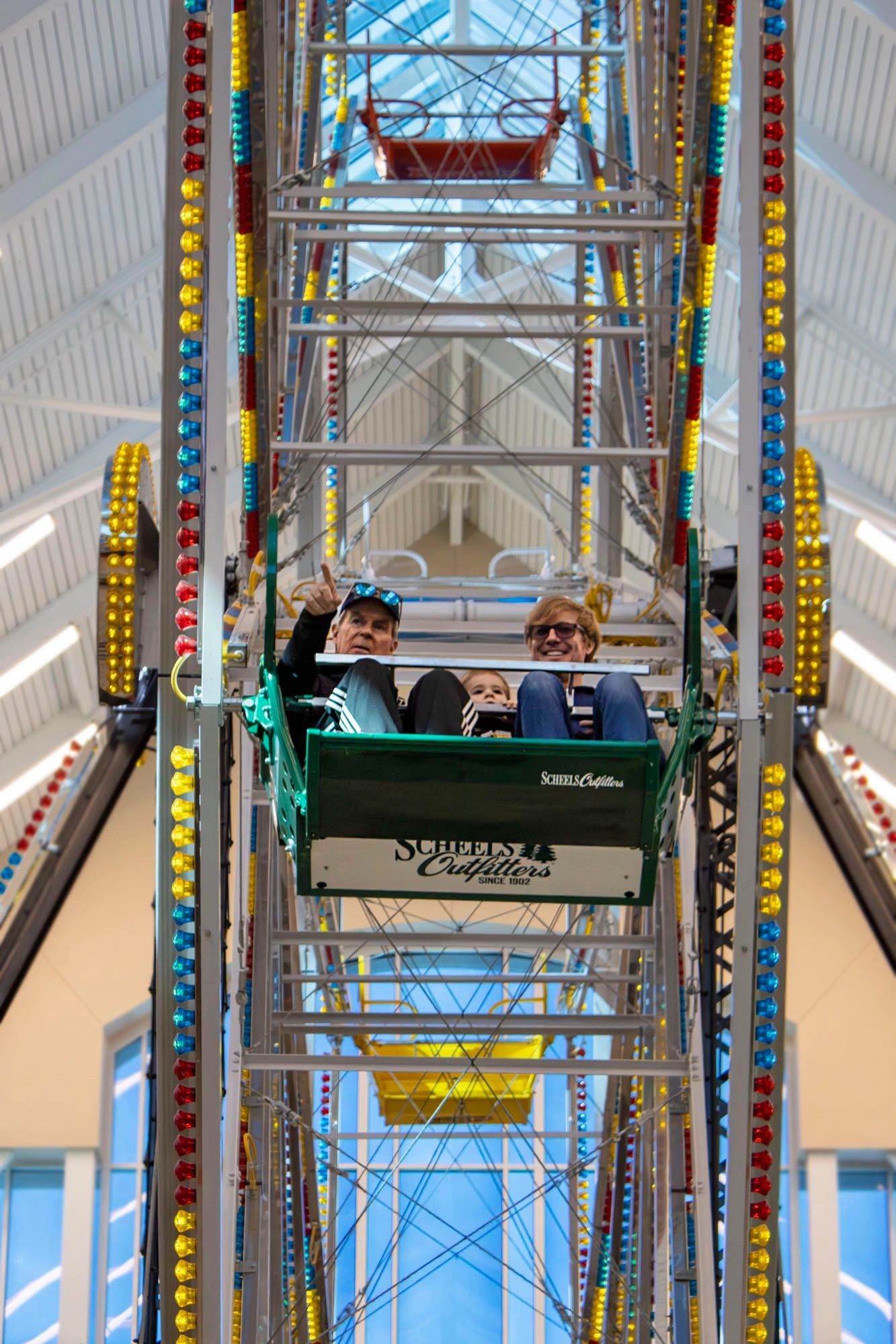 Three people enjoying a Ferris wheel ride indoors at Scheels Outfitters.