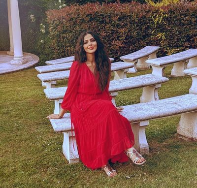 A woman in a red dress sitting on a white bench in a garden.