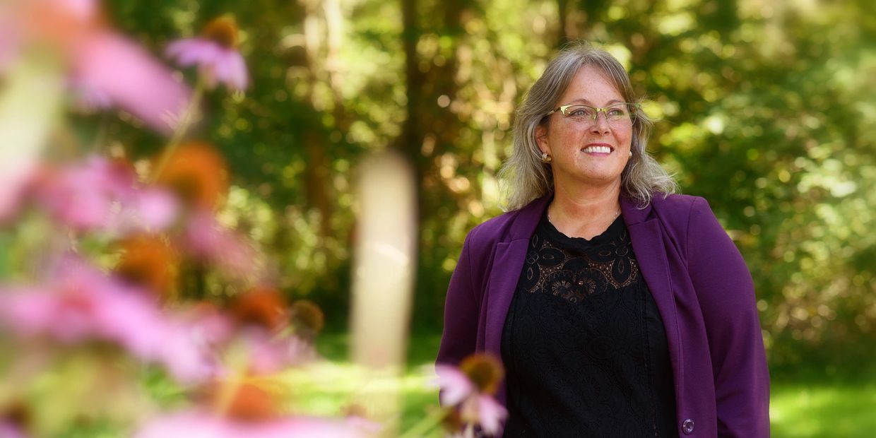 Vikki Poirier smiling in a garden with flowers.