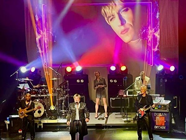 A live band performs on stage with vibrant lighting and a large screen projection.