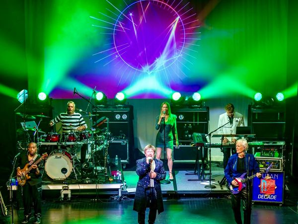 Live band performing on stage with vibrant green and purple lighting.