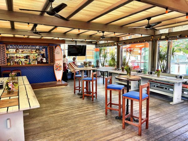 Bright beachside bar with wooden floors and colorful stools.
