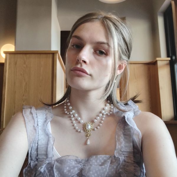 Young woman with pearl necklace and ruffled dress in cozy indoor setting.