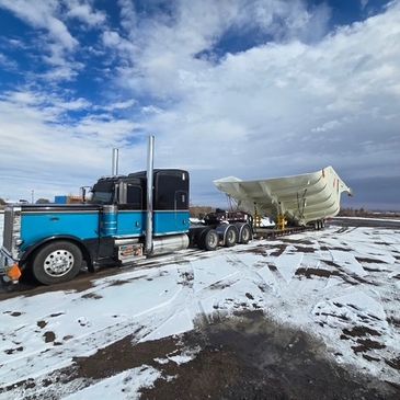 Blue and black semi-truck hauling a large white boat on a snowy road.