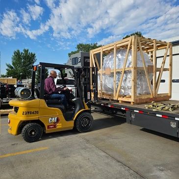 Man operating forklift to load a large crate onto a truck.