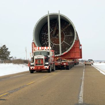 A large truck transports an enormous cylindrical industrial component on a snowy road.