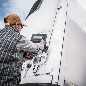 Man in a cap operates control panel on a large white truck.