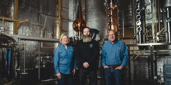 Three people standing in a distillery.