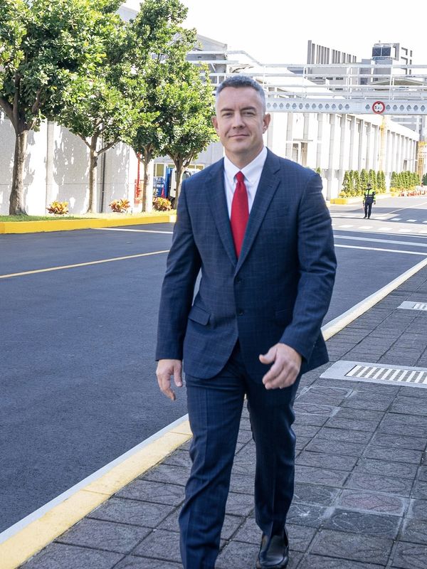 Man in a suit walking on a sidewalk near a road.