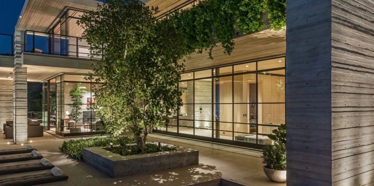 Modern house exterior with large windows and a tree in a concrete planter at night.