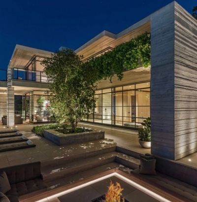 Modern two-story house with large windows and outdoor fire pit at night.