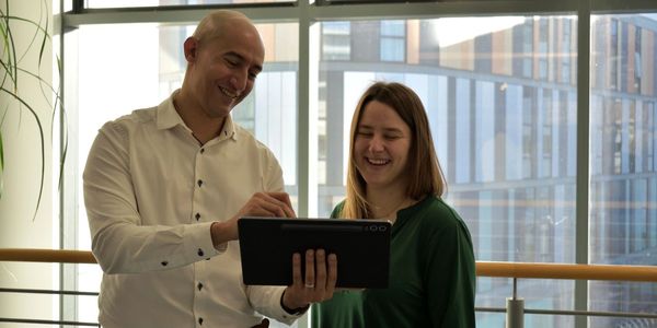 Two colleagues smiling while looking at a tablet in a modern office.