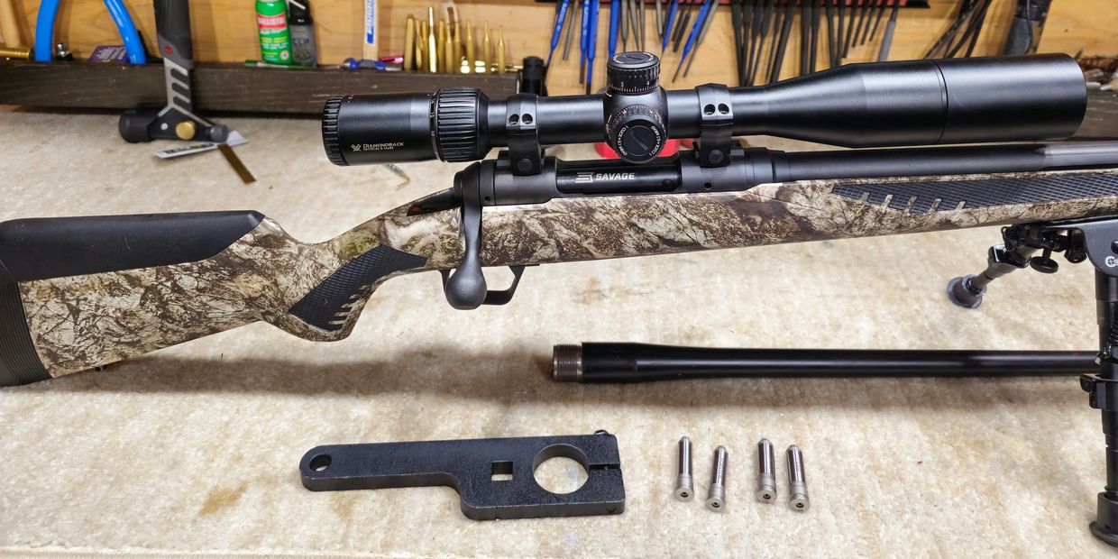 Savage rifle with scope and accessories on a table.