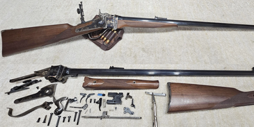 Disassembled and assembled old-fashioned rifles with wooden stocks.