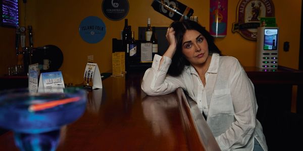 Woman in white shirt sitting pensively at a bar counter.