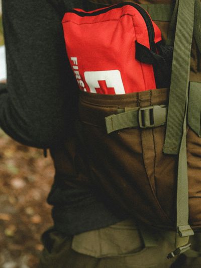 Red first aid kit in a brown backpack pocket outdoors.
