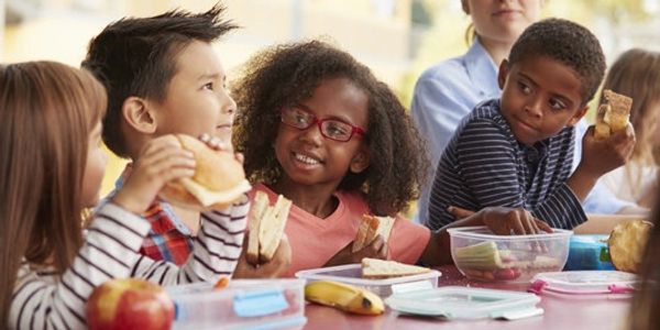 Children eating lunch together at a school table, sharing sandwiches and snacks.