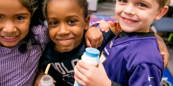 Three children smiling and holding milk bottles together.