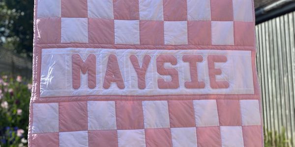 Traditional square patchwork quilt in pink and white with name in centre.
