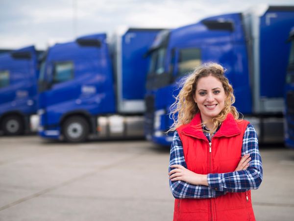 Portrait of woman truck driver in casual clothes standing in front of truck vehicles