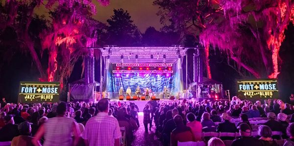 Outdoor jazz and blues concert at Fort Mose with colorful lighting and a large audience.