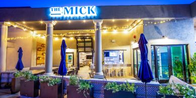 Outdoor evening view of The Mick restaurant with string lights and blue umbrellas.