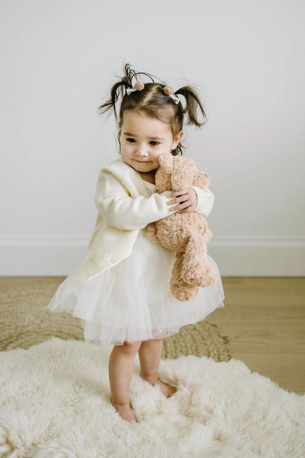 baby girl holding bear in white tutu dress and sweater