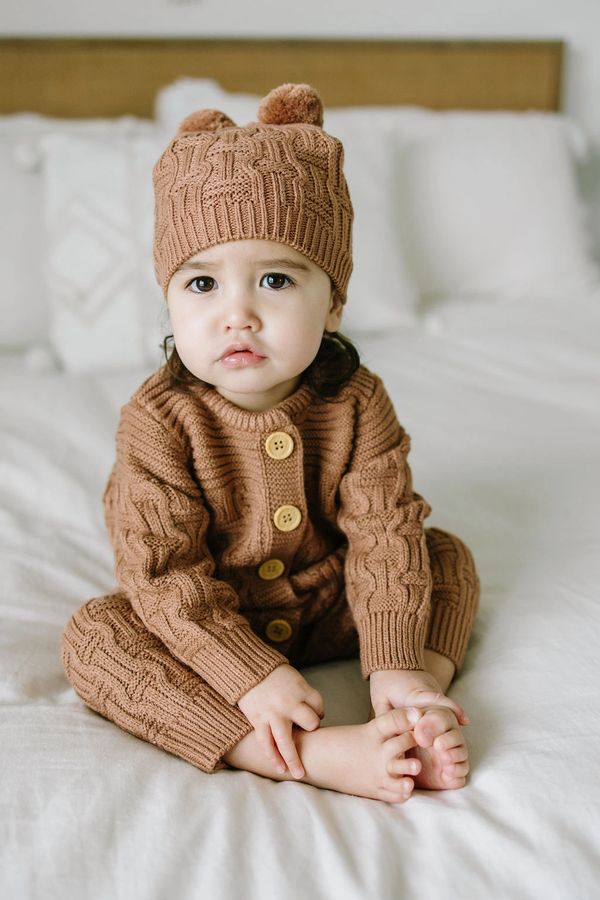 baby sitting on bed in sweater onesie and matching hat set