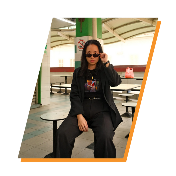 Confident woman in black outfit adjusting sunglasses while sitting indoors.