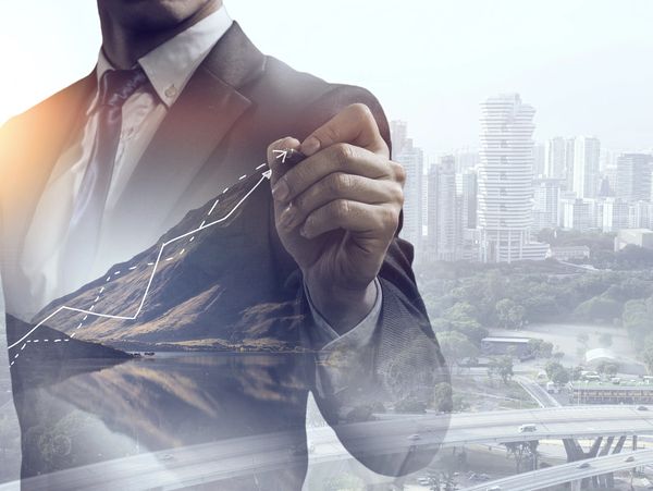 Businessman drawing an upward graph with cityscape background.
