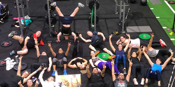 Group of gym members posing playfully on the floor post-workout, showing team spirit and hard work.