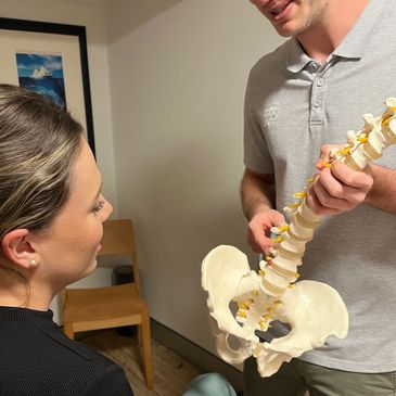 Mobile chiropractor Jack Worthington holding a spine model, explaining spinal anatomy to a patient.