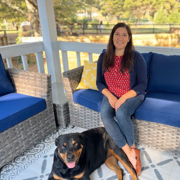 Woman sitting on a porch sofa with a large black and tan dog lying on the floor.