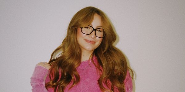 Smiling woman with red hair and glasses in a pink sweater.