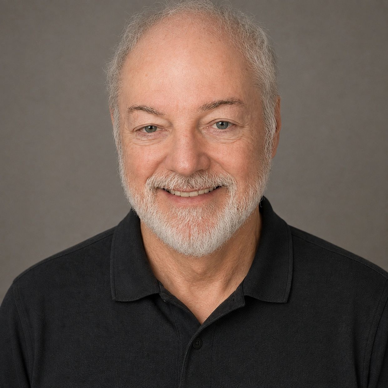 Smiling elderly man with white hair and beard in a black polo shirt.