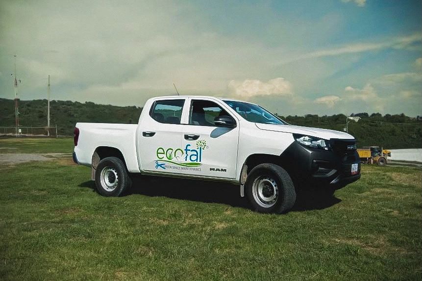 Camioneta blanca de ecofai en campo verde bajo cielo nublado.