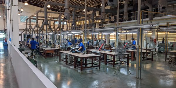 Workers in blue uniforms operate machinery in a spacious factory workshop.