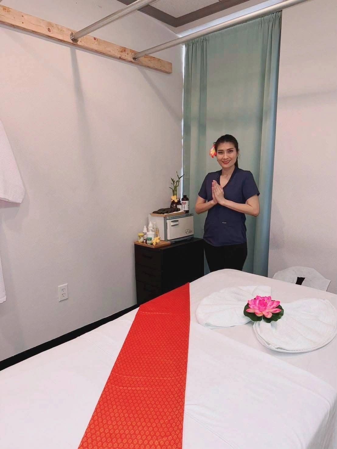 Smiling woman in a massage room with hands in a greeting gesture.
