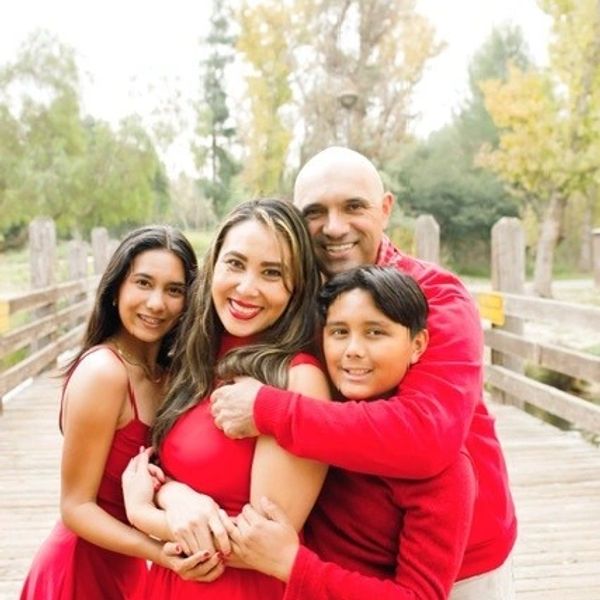 A happy family of four dressed in red poses on a wooden bridge outdoors.