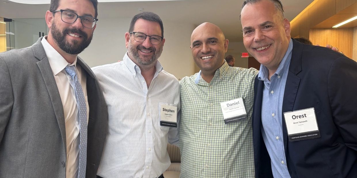 Four men smiling at a professional event, wearing name tags and business attire.
