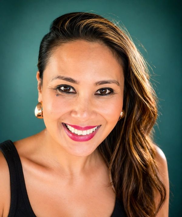 Smiling woman with long hair and gold earrings against a teal background.