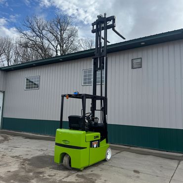Bright green forklift with extended mast beside a building on a cloudy day.