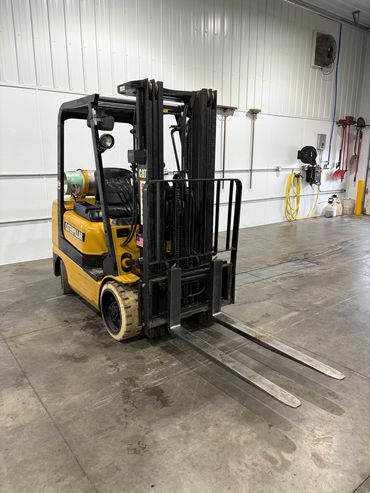Yellow Caterpillar forklift parked inside a warehouse with concrete flooring.