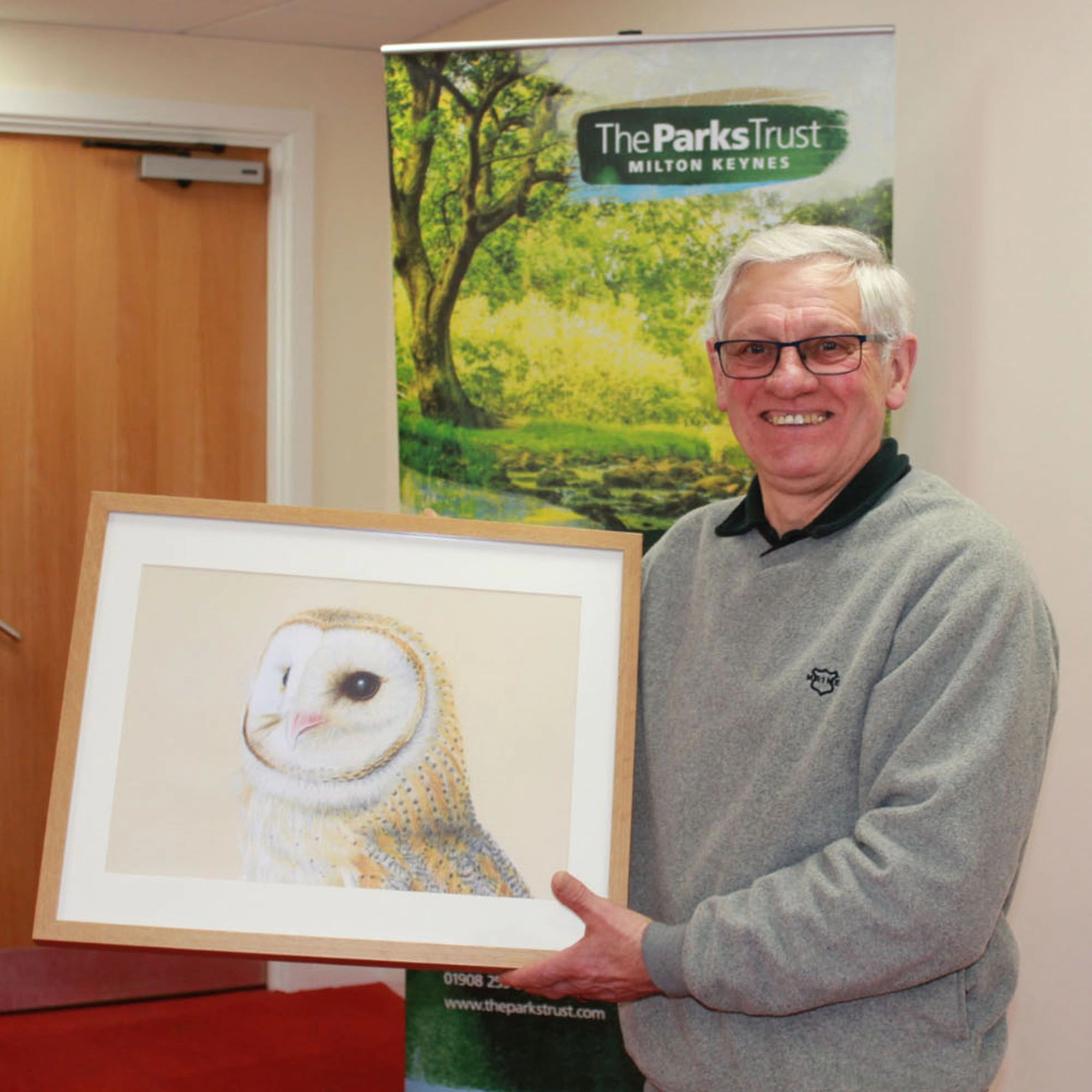 Elderly man holding framed owl artwork.
