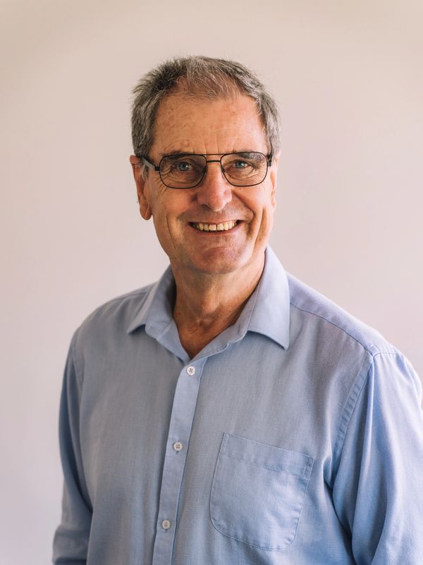 Smiling elderly man wearing glasses and a light blue shirt.