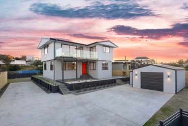 Modern two-story house with a red door and detached garage at sunset.