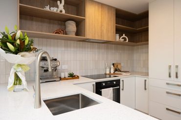 Modern kitchen with white countertops and wooden shelves.