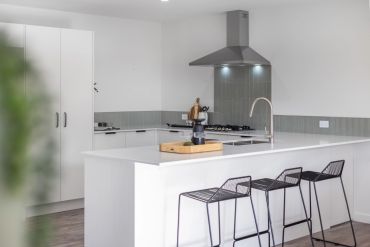 Modern kitchen with white island and black wire stools.
