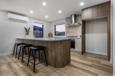 Modern kitchen with wooden island and black bar stools under bright recessed lighting.