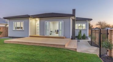 Modern single-story house with a wooden deck and green lawn.
